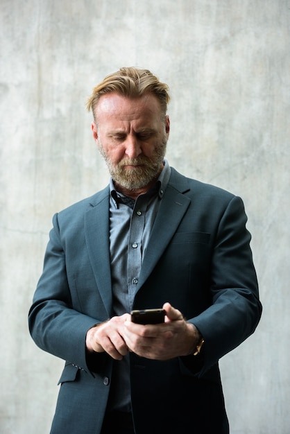 Portrait of mature handsome bearded businessman with blond hair in suit against concrete wall outdoors