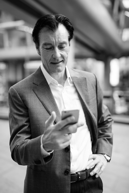 Portrait of mature handsome businessman exploring around the city in black and white