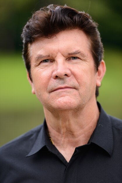 Portrait of mature handsome businessman relaxing at the park outdoors