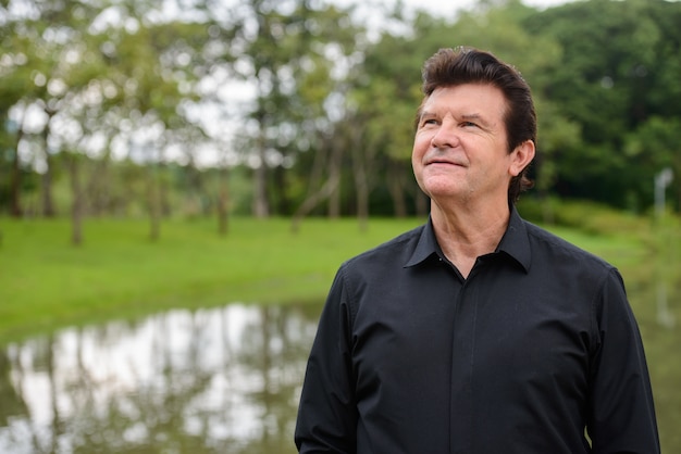 Portrait of mature handsome businessman relaxing at the park outdoors