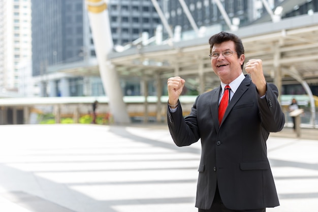 Portrait of mature handsome businessman wearing suit in the city outdoors