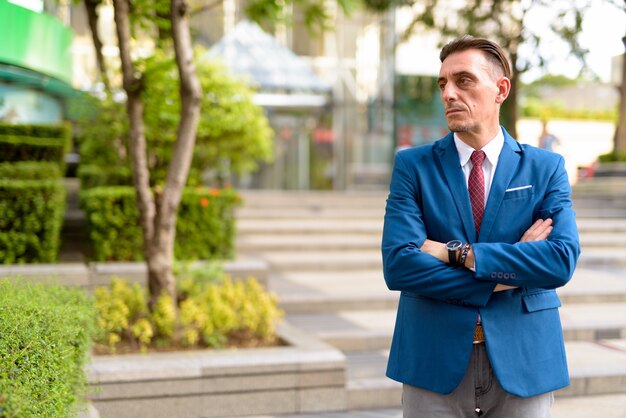 Portrait of mature handsome Italian businessman relaxing outside of the building