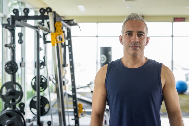 Portrait of mature handsome Persian man with gray hair exercising at the gym