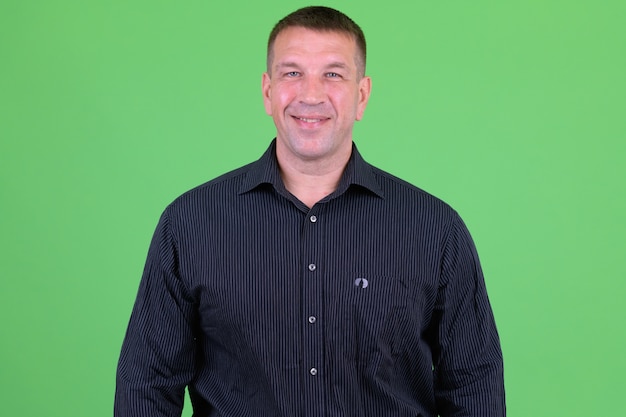 Portrait of mature macho businessman against chroma key with green wall