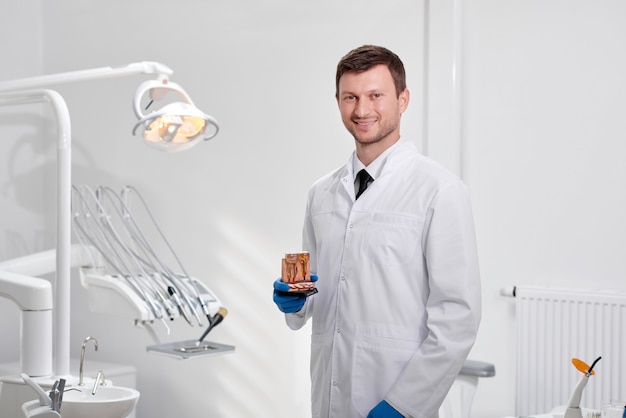 Portrait of a mature male dentist posing proudly at his clinic holding teeth model smiling to the camera copyspace profession occupation experience trust medicine health dentistry oral examination.