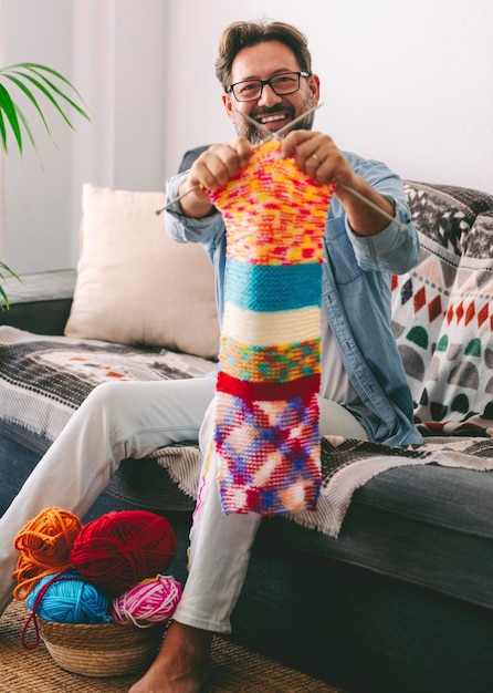 Il ritratto del maschio maturo mostra con orgoglio il suo risultato di lavoro a maglia con un grande sorriso uomo felice che mostra i vestiti dell'indumento di lana fatti a mano da lui stesso attività di hobby e tempo libero stile di vita delle persone a casa inverno