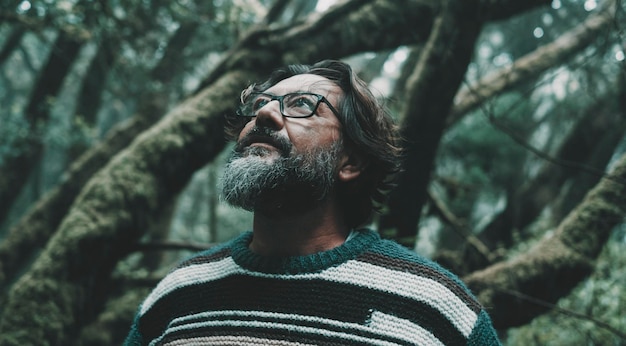 Portrait of mature man looking up with forest woods trees green ambient in background Close up of male people in nature outdoors park leisure activity Beard and eyeglasses Life balance environment