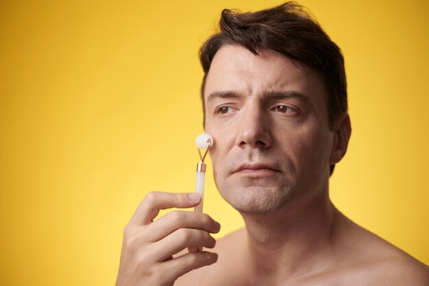 Portrait of mature man massaging face with rose quartz roller after morning shower