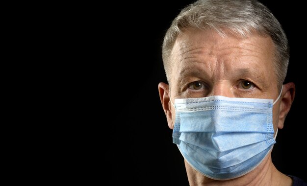 Portrait of mature man in medical mask looking at camera on black background