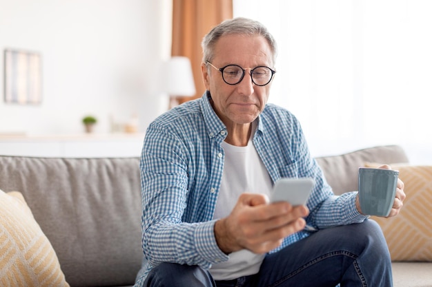 コーヒーを飲むスマートフォンを使用して成熟した男の肖像画