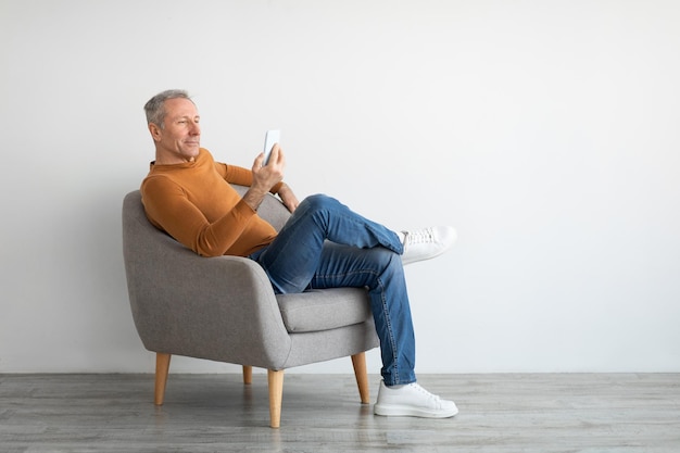 Portrait of mature man using smartphone sitting on armchair