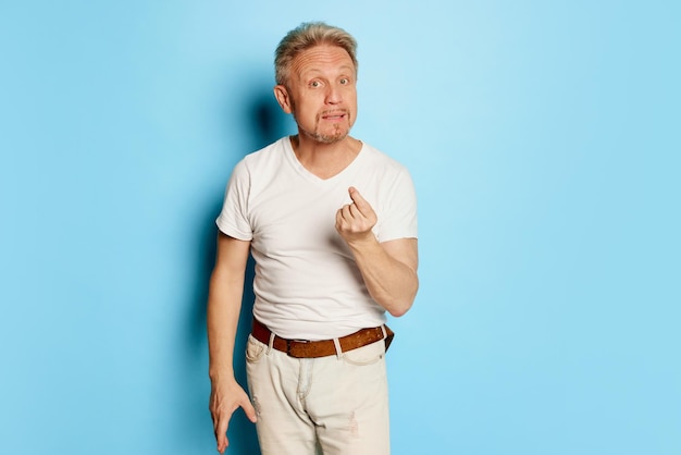 Portrait of mature man in white tshirt posing isolated over blue studio background arguing face
