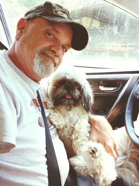 Photo portrait of mature man with dog sitting in car