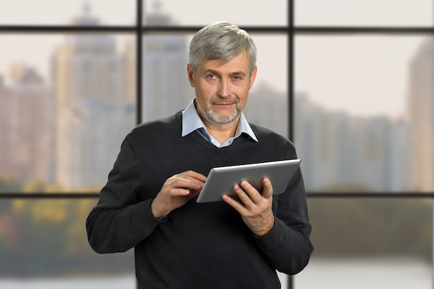 Portrait of mature man with pc tablet. Serious grey hair man holding computer tablet on office window close up