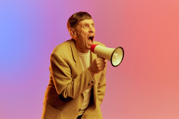 Portrait of mature middleaged man in jacket posing shouting in megaphone over gradient pink purple