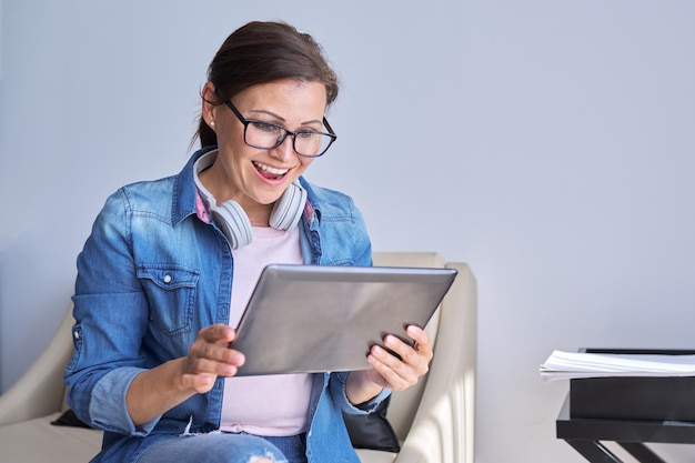 Portrait of mature smiling woman looking at monitor of digital tablet talking female sitting at home communicates online with friends family business colleagues chatting using video call copy space