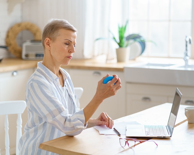 Portrait of mature woman exercising with rubber round grip ring while working online from home