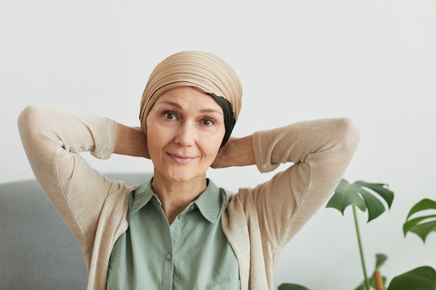 Portrait of mature woman looking at camera while putting on headscarf at home and getting ready to go out, copy space