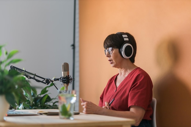 Photo portrait of mature woman wearing headphones and talking at online radio station podcast and broadcast concept