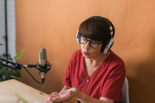 Portrait of mature woman wearing headphones and talking at\
online radio station podcast and