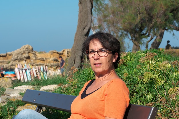 Portrait of a mature woman with eyeglasses, sitting on a bench 