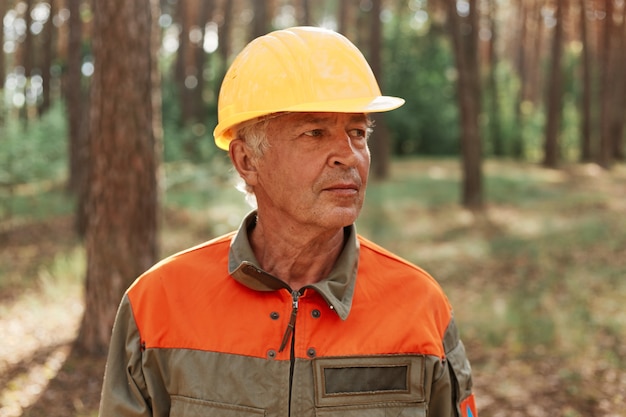 Foto ritratto di boscaiolo maturo in posa nella foresta all'aria aperta e distoglie lo sguardo con espressione pensierosa