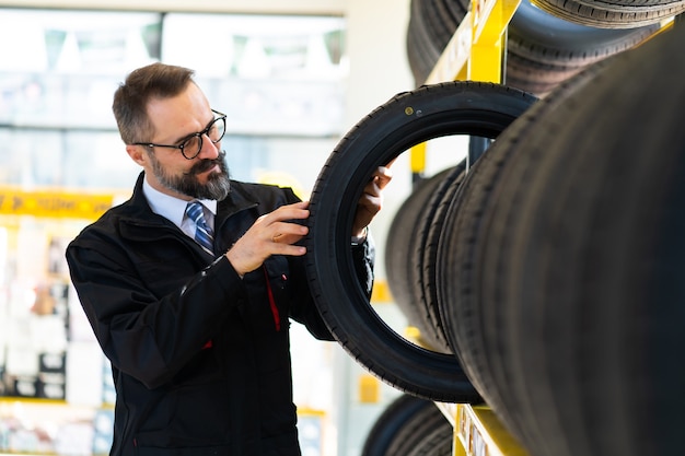 Portrait of Mechanic man with car tires at service station. Male mechanic holding car tire in automobile store shop