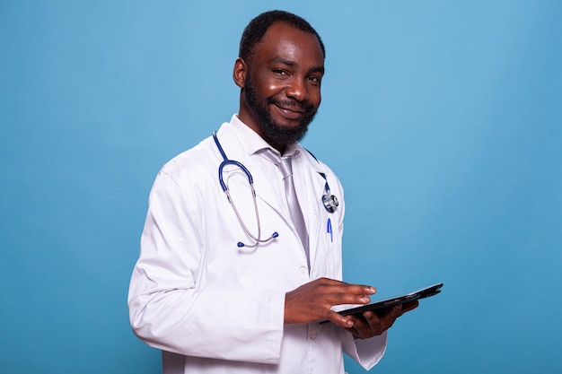 portrait of medical doctor with stethoscope smiling at camera holding touchscreen tablet wearing hospital uniform. happy medic in lab coat using digital device.