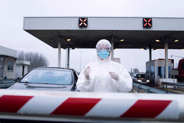 Portrait of medical heath care worker in protective white suit with gloves standing at checkpoint and holding test kit for covid-19.