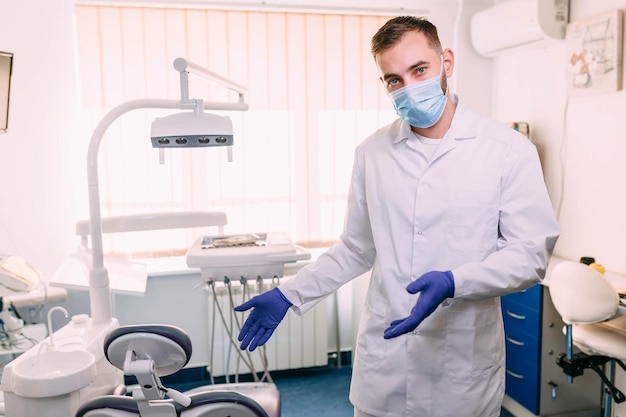 Portrait of a medical specialist in a surgical mask and uniform points to armchairs