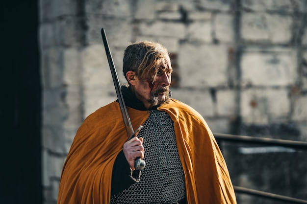 Портрет средневекового старшего воина в доспехах после битвы с кровью на лице. Воин держит меч в руках