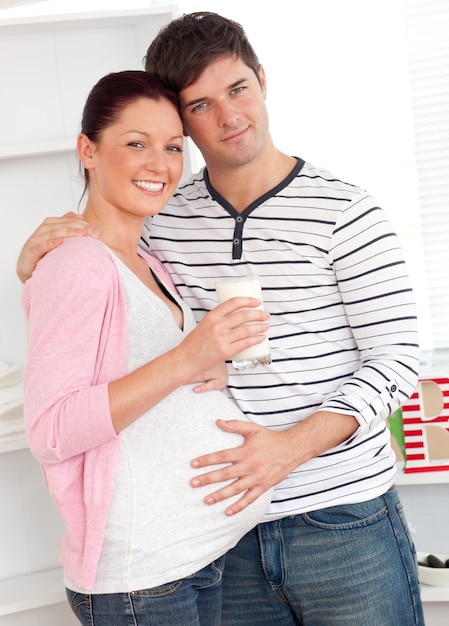 Portrait of a merry pregnant woman holding a glass of milk and of her husband touching her belly