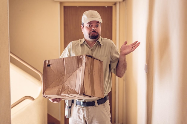 portrait of messenger with cardboard box standing in building
