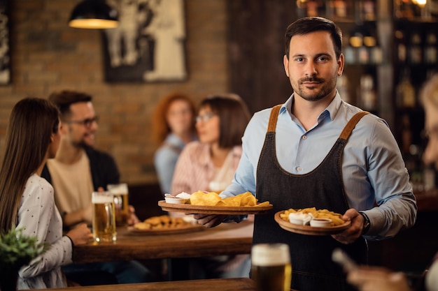 Portrait of mid adult waiter serving food to guests in a tavern and looking at camera