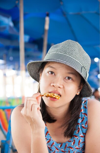 Portrait of mid adult woman eating food looking away while sitting against parasols