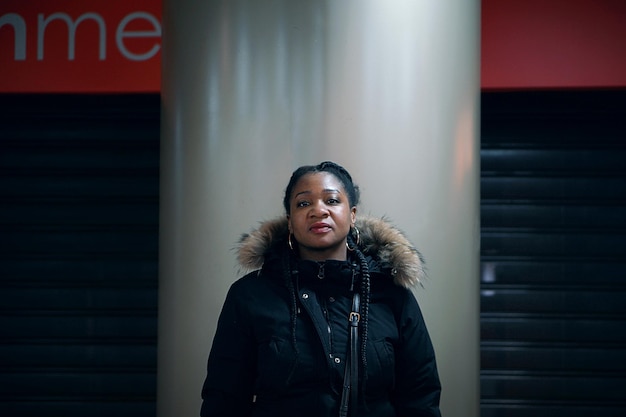 Photo portrait of mid adult woman wearing hooded jacket standing against silver column