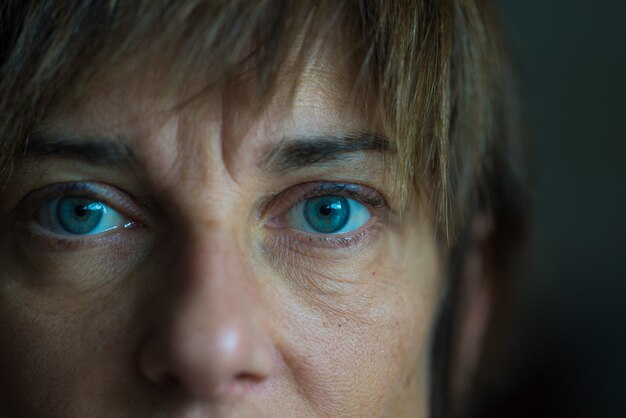 Portrait of mid aged woman with blue eyes, close up and selective focus on one eye, very shallow depth of field. Dark setting, toned image.