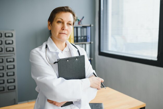 中年女性医師の肖像画は彼女の首に聴診器で白衣を着ています