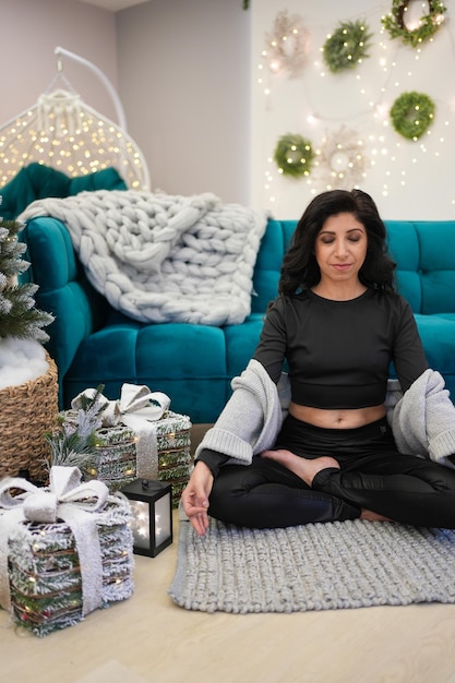 Portrait of middle age woman meditating while sitting near sofa and christmas tree