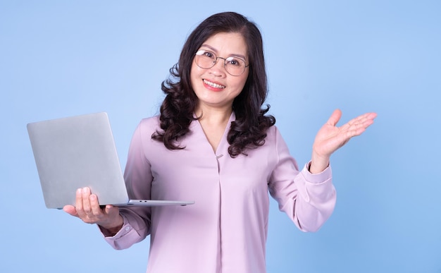 Portrait of middle aged Asian woman using laptop on blue background