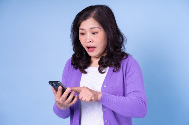 Portrait of middle aged Asian woman using smartphone on blue background