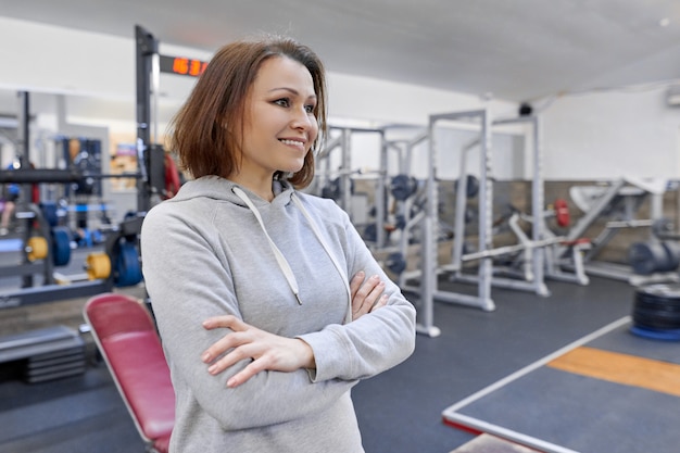 Portrait of middle-aged confident woman with folded hands in gym