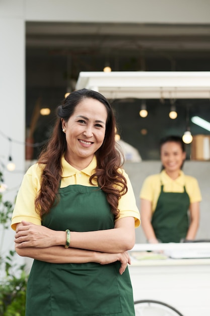 Portrait of middle-aged food cart vendor crossing arms and smiling at camera