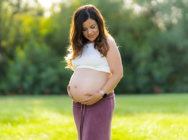 Portrait of a middle-aged pregnant latina woman embracing her abdomen while looking down