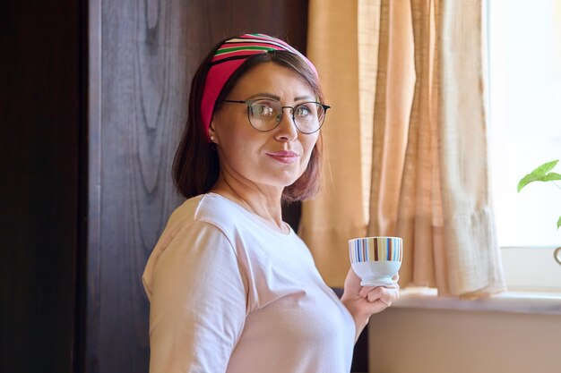Портрет женщины средних лет дома на кухне с чашкой кофе