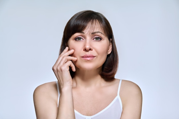 Portrait of middle aged woman looking at camera on light studio background