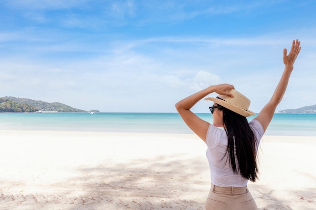 青い海と空を見渡す白いTシャツと帽子で立つ女性の肖像画のミディアムショットビュー