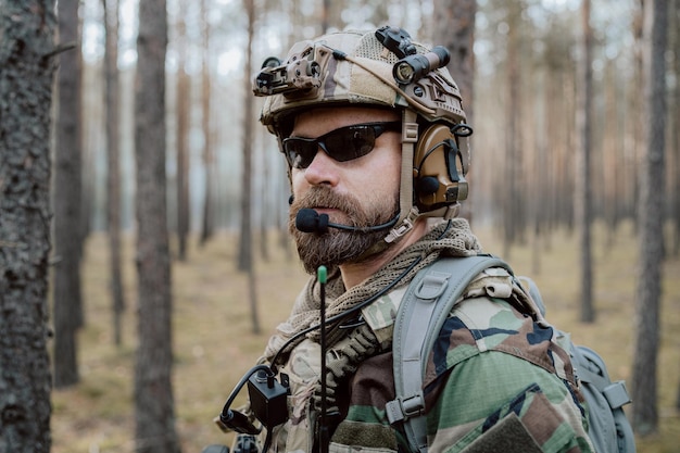 Portrait of a middleaged bearded soldier in a woodland military uniform and helmet with headphones