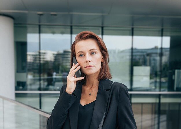 Photo portrait of a middleaged female with ginger hair talking on her mobile phone while standing outdoors