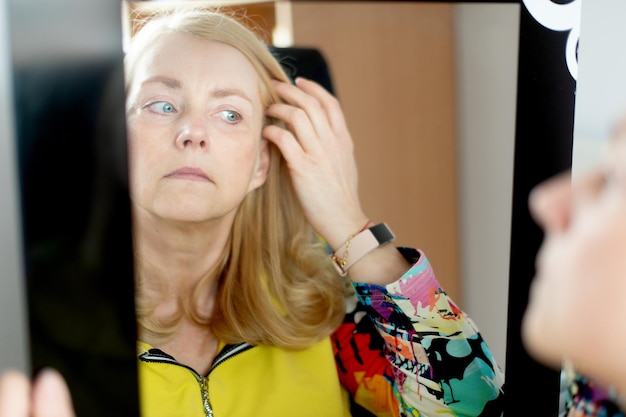 Portrait of middleaged woman looking at her face in mirror skin\
aging concept